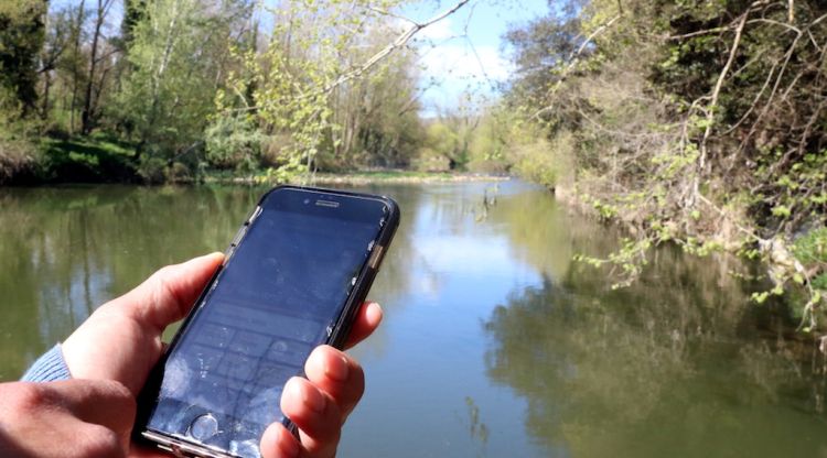 Un mòbil amb l'aplicació de la Ruta del Ter i, de fons, el riu al seu pas per Sant Julià de Ramis. ACN
