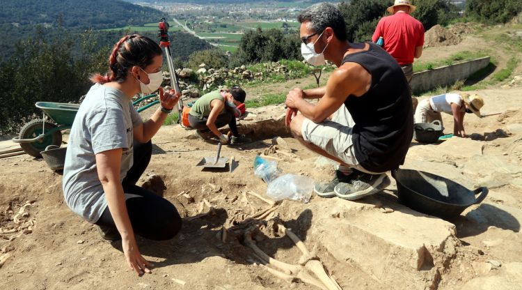Els codirectors de l'excavació als Sants Metges, Neus Coromina i Jordi Vivo, al costat d'un dels esquelets. ACN