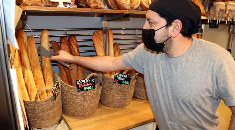 Un forner agafa una barra de pa a la fleca de 'La Rovira' a la plaça Rovira i Trias de Barcelona. ACN