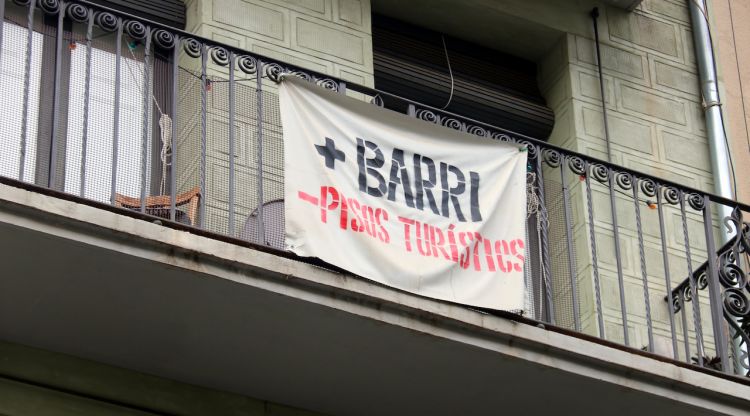 Detall d'un cartell amb el lema '+Barri -Pisos Turístics' en un balcó de la Rambla de Girona. ACN